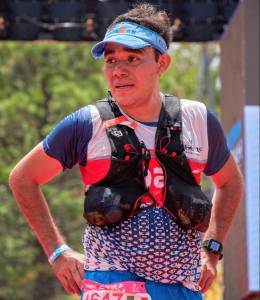 Runner at Ultra Coahuila race. The runner is wearing a blue visor, hydration pack, and race bib, looking determined with a background of trees.