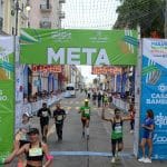 Runners crossing the finish line at the Veracruz Marathon 2022. The event banner reads "META" and displays finish times. Spectators and staff line the route, cheering on the athletes. An Oax Sport runner in a green shirt raises his arms in victory.