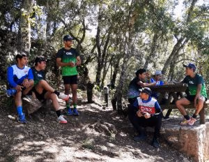 Athletes sitting and standing around a picnic table, taking a break during a trail run in a forest.