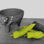 Green chilies next to a black stone molcajete and pestle.
