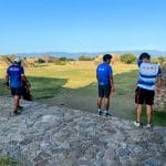Tres personas caminando en la zona arqueológica de Monte Albán, Oaxaca, México, usando camisetas deportivas.