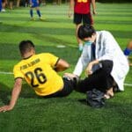 Jugador de fútbol recibiendo atención médica en el campo por parte de un profesional de la salud durante un partido nocturno.