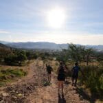 Runners on a rocky trail with the sun rising over the hills, casting long shadows as they head towards the valley during the Monte Alban Sunrise Run in Oaxaca.
