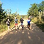 Anaya from England in black, Charlie in green from Georgia, Ollie Bishop from England in black, and Luis Fabian Santiago in blue running on a dirt path surrounded by greenery during the Monte Alban Sunrise Run in Oaxaca.