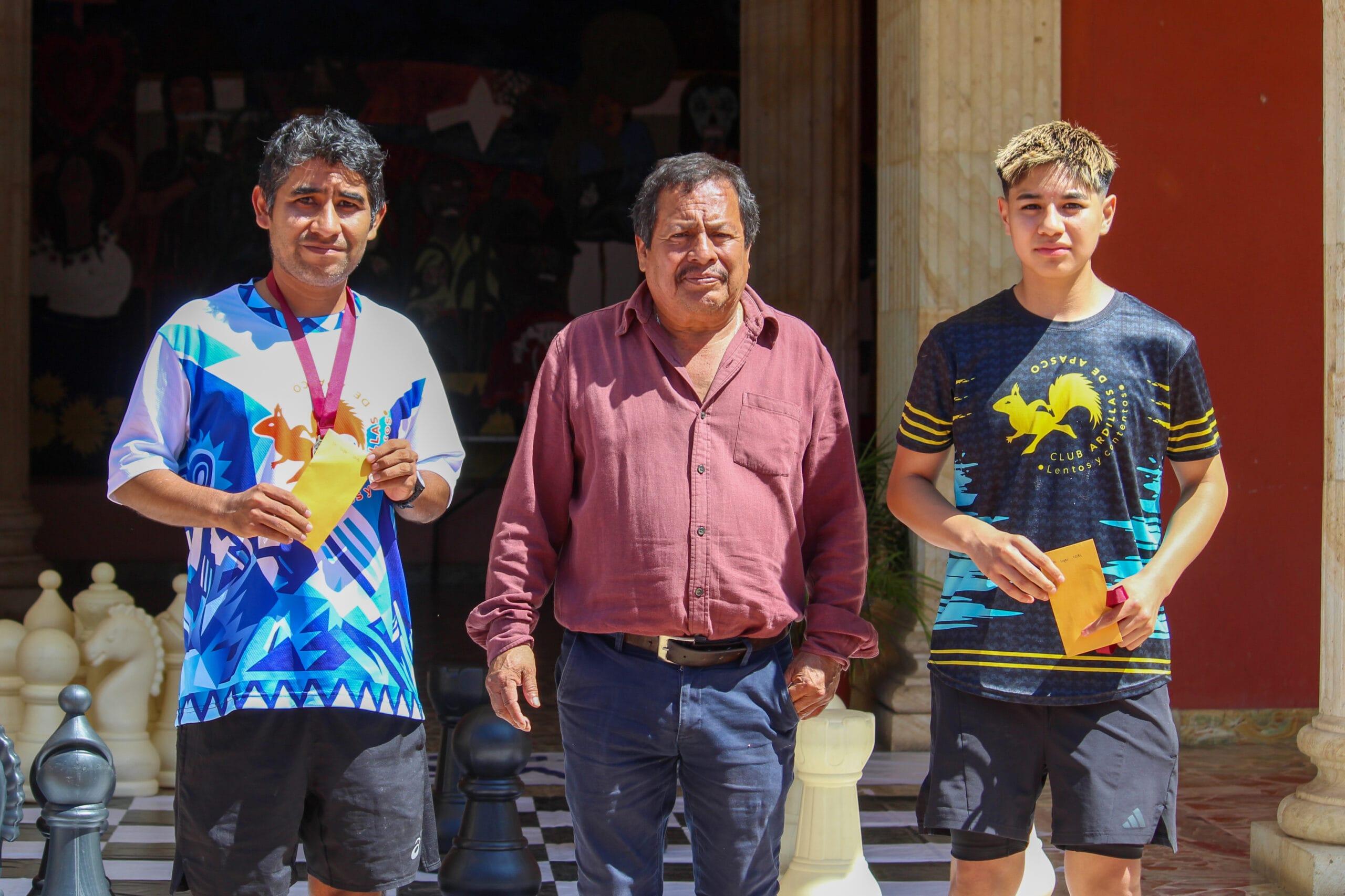 Dos corredores sostienen sus sobres de premiación junto a una autoridad municipal después de la ceremonia de Senderos de Cantera.