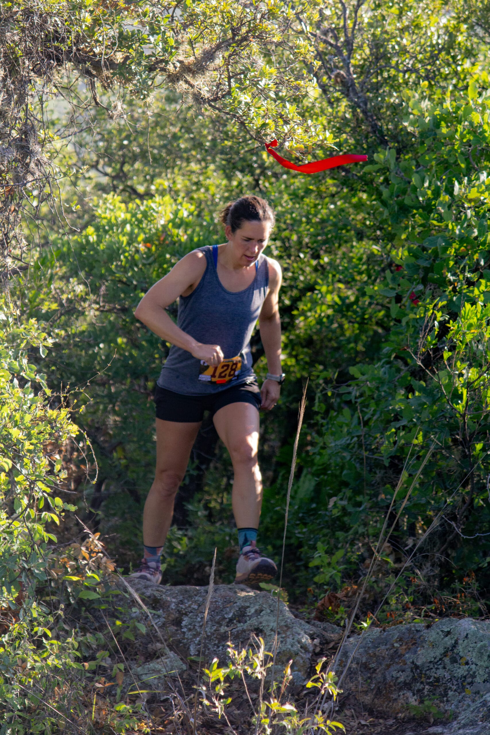 Katie avanza por un sendero rocoso debajo de una cinta roja que marca la ruta de Senderos de Cantera 12K.