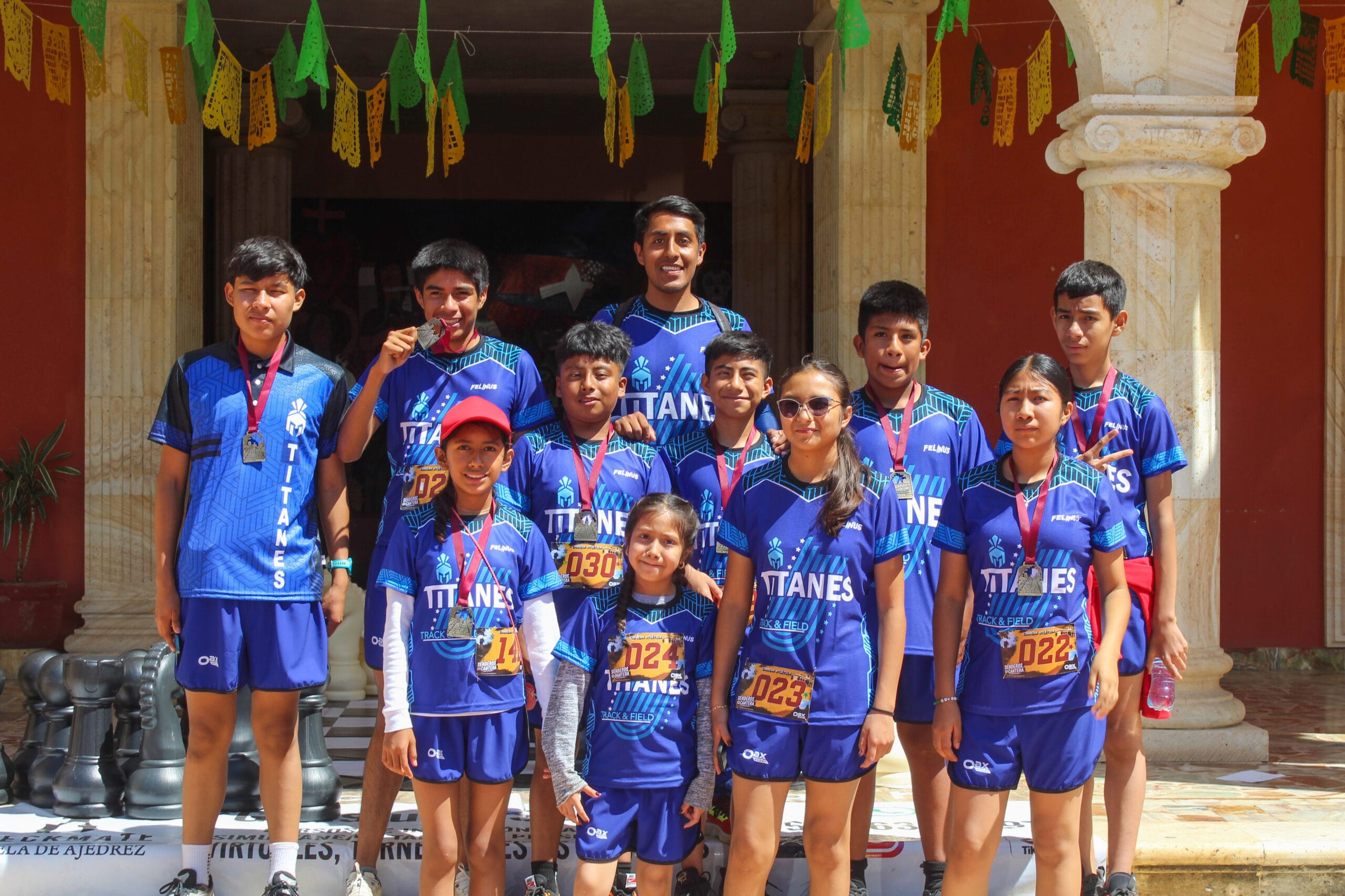 Jóvenes atletas de Magdalena Apazco, con kits azules para correr y medallas, posan después de Senderos de Cantera 12K.