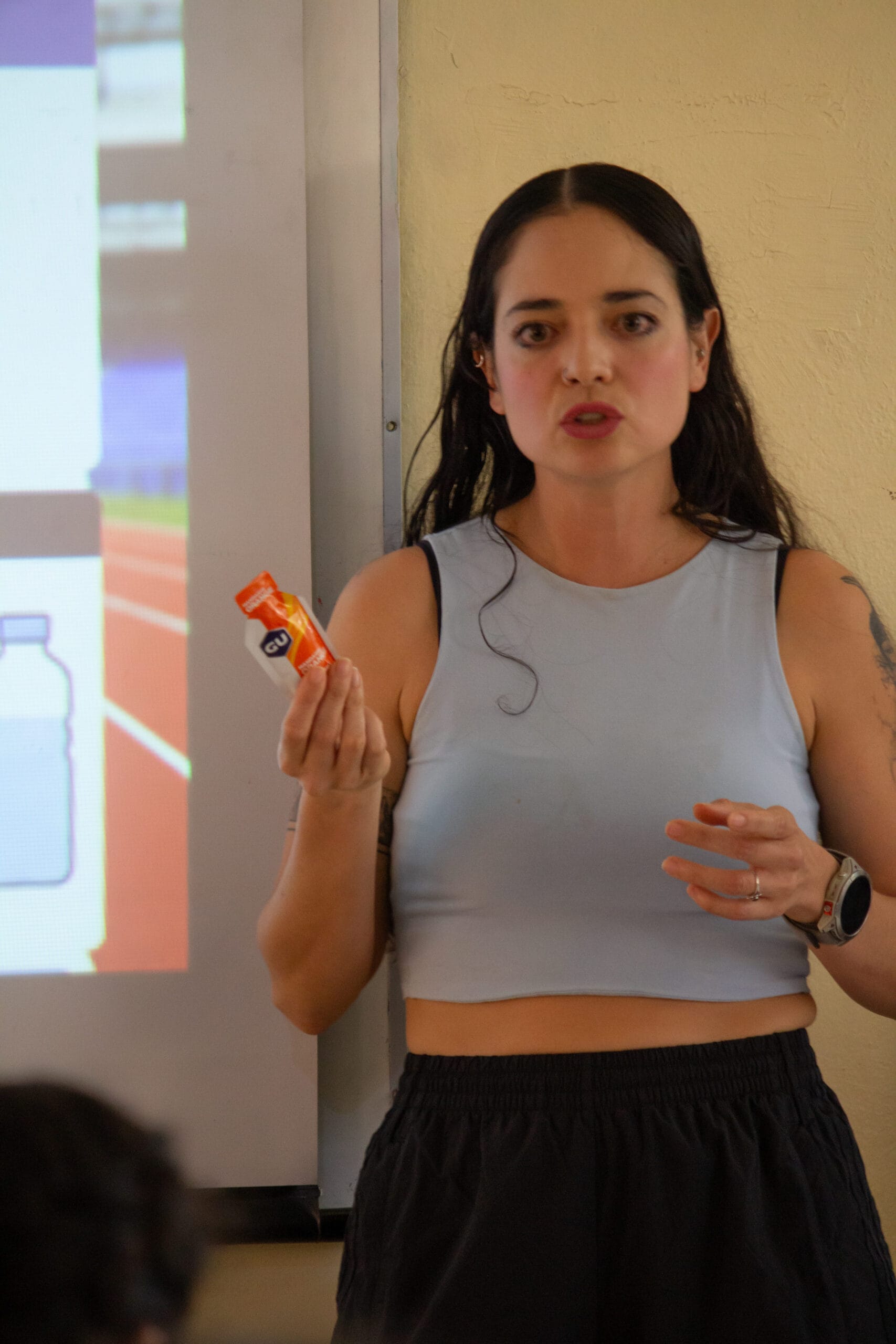 Especialista en nutrición deportiva sosteniendo un gel energético GU mientras habla con los participantes del campamento.