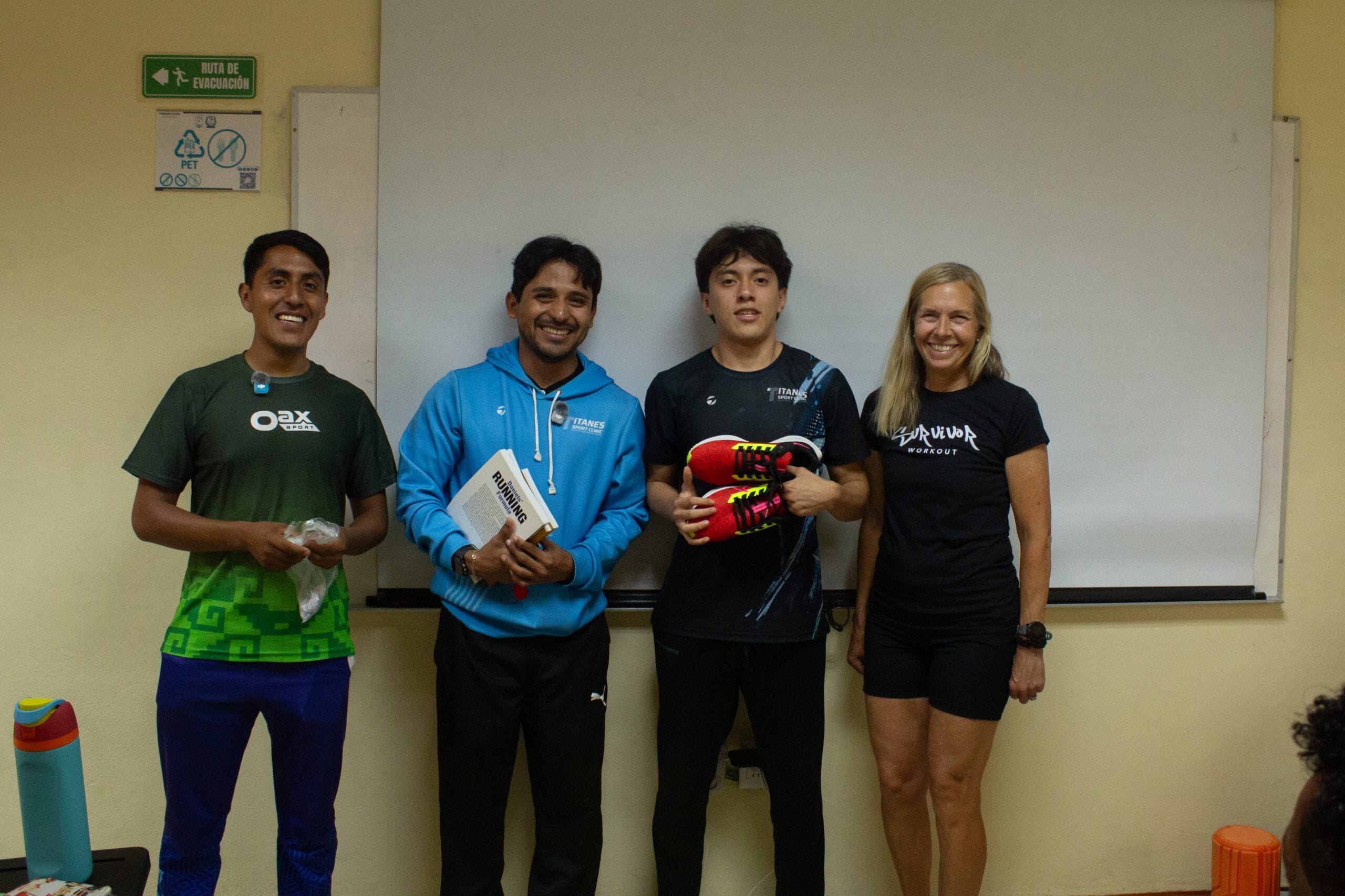 Cuatro participantes y organizadores del campamento posando con calzado para correr y libros de entrenamiento durante las actividades de clausura.