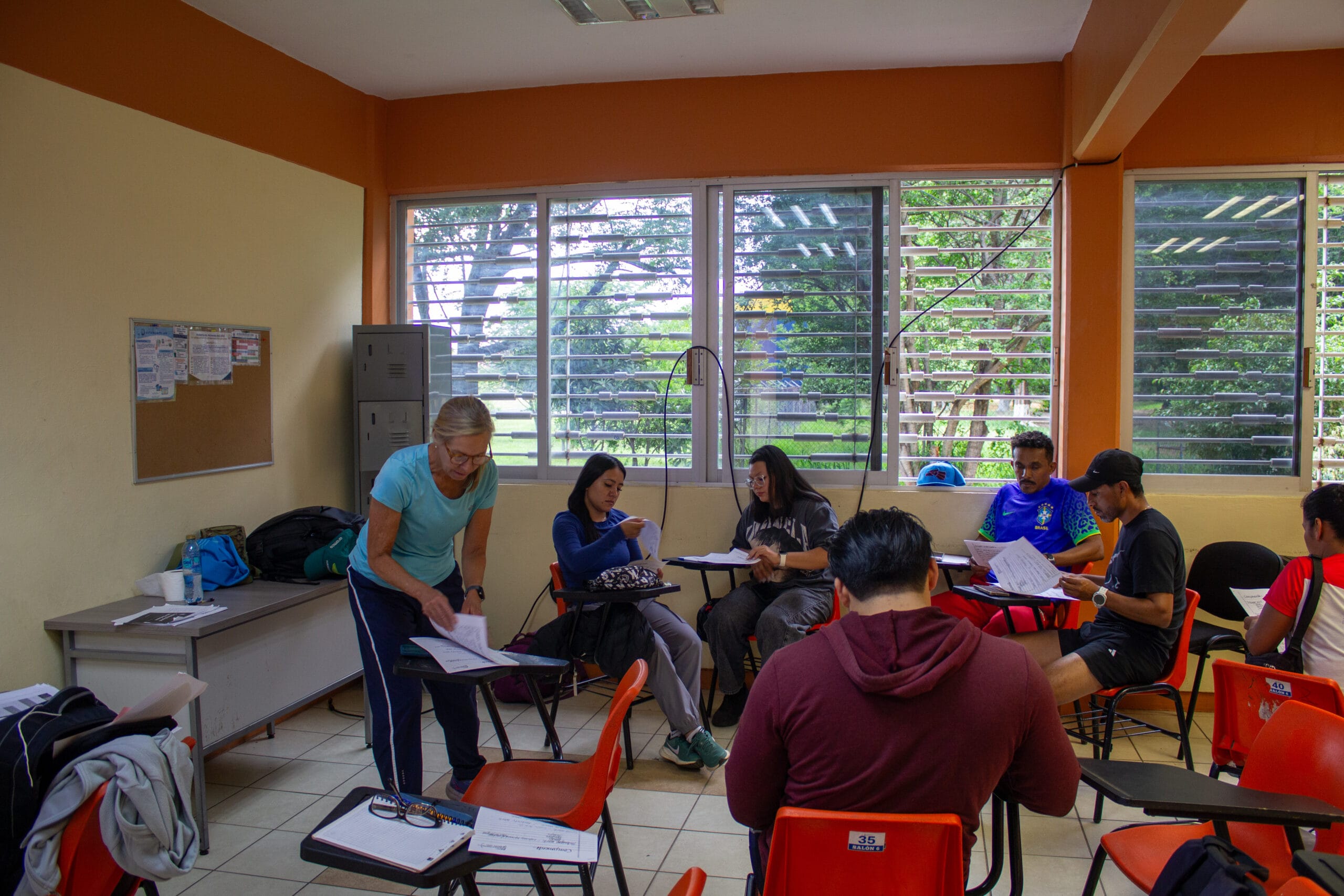 Atletas, entrenadores y estudiantes trabajando en grupos pequeños con planes impresos durante un taller en el aula.