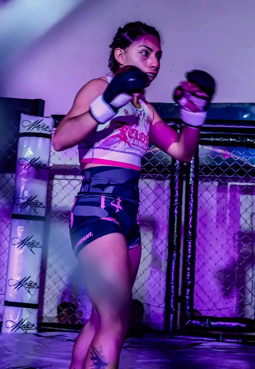 Emily Barrera en guardia, con los guantes levantados, dentro de una jaula de MMA con luz morada.